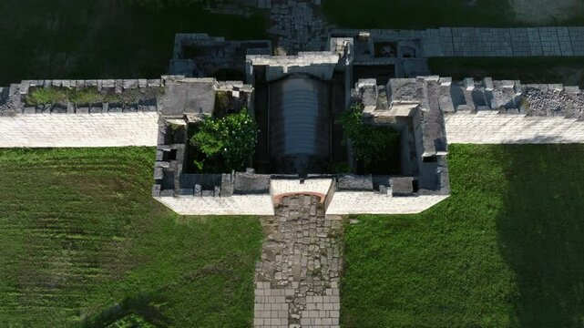 A fortified entrance wall and a tree-lined path mark the entrance to the historic city of Pliska, stretching through open grasslands in Bulgaria.