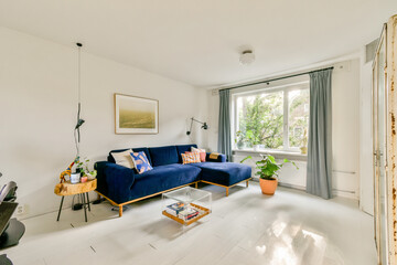 A bright and inviting modern living room featuring a blue sofa, natural light from a window, and...