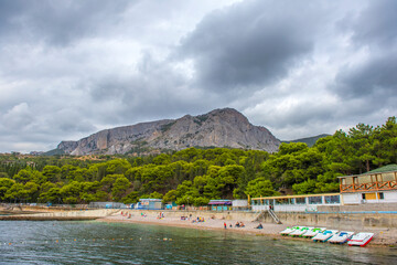 Fototapeta premium picturesque beach in Foros, Crimea. In the foreground is calm sea water with buoys, pebbles and a row of catamarans. 
