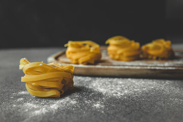 Raw nests of fettuccine pasta arranged on a light surface with a dark textured background. Minimalist food composition highlighting traditional Italian ingredients