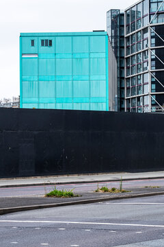 Minimalist view of turquoise modular building next to black construction wall and empty road, reflecting urban contrast, geometry and pending development.