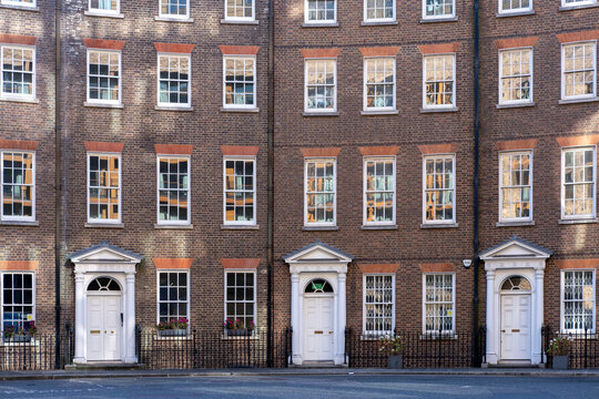 Historic row of Georgian townhouses with white doors and aligned windows, captured frontally under balanced light, emphasizing classic architecture and urban symmetry.