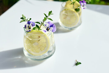 Iced lemonade with edible pansy flowers, lime and mayran. Refreshing summer drink. Healthy organic summer soda drink. Detox water. Diet unalcolic coctail.