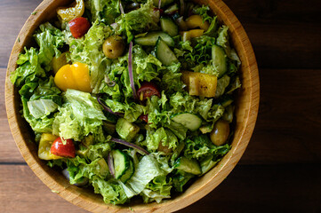 Fresh vegetable salad in a wooden bowl with cherry tomatoes, cucumber, bell pepper, avocado, red onion, greens and olives. Healthy colorful dinner, Mediterranean family meal.