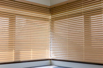 Corner view of beige wooden blinds meeting at a right angle. Light softly filters through the slats...