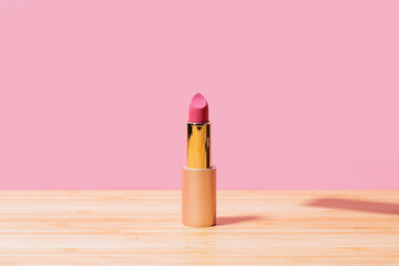 Pink lipstick on wooden table against pink background