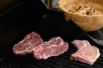 Fresh marinated steaks being placed on a hot gas grill with metal tongs. Juicy raw beef with salt, pepper, and oil. Outdoor BBQ, cooking preparation, close-up food shot.