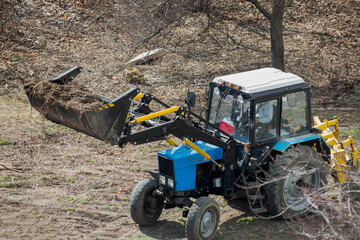 Obraz premium The construction loader with an elevated bucket, carrying debris and wood waste, is clearing the area. Landscaping work is in progress.