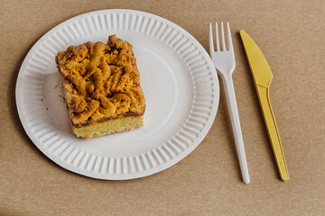 A top view of a pie on a white plate on a sandy background. Simple serving with disposable utensils, recipes for homemade baking, and a calorie-rich breakfast.