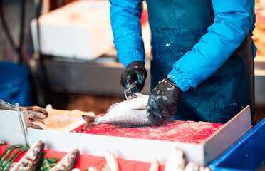 Fishmonger cleaning fresh fish at a market stall. The fish is suitable for fasting meals, ideal for traditional dishes during Lent or religious fasting.