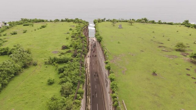 Aerial tracking shot over the famous Tanah Barak cliff and lush grassy field, leading to the hidden Pandawa Beach in Bali, Indonesia. Stunning coastal views of this viral natural wonder.