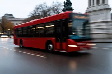 Selbstklebende Fototapeten Bright red bus speeds through wet city streets, showcasing urban © Anna