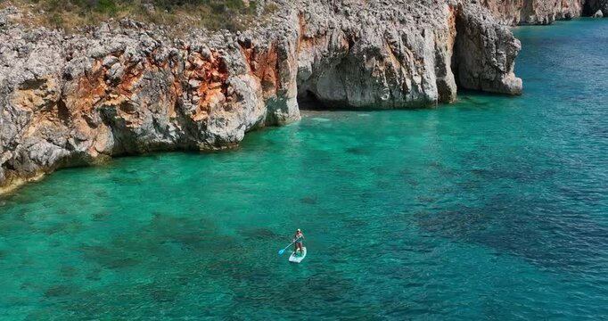 Orbit drone shot of Canyon of Gjipe with caucasian woman doing paddle on the Ionian Sea during the day in Vlore County, Albania