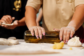The housewife rolls out the dough with a wine bottle