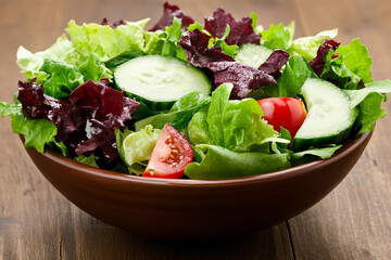 Fresh mixed vegetable salad featuring leafy greens with cucumbers and tomatoes served in a rustic bowl