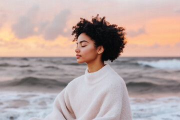 A woman sits peacefully by the shoreline, meditating as the sun sets. The soft waves crash around her while vibrant colors fill the sky