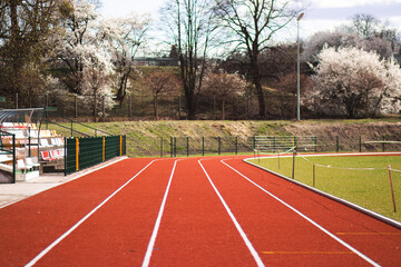 Red running track at an athletics stadium. Clean textured rubber surface with white lines, photographed in natural daylight. Sports infrastructure for training and competitions.

