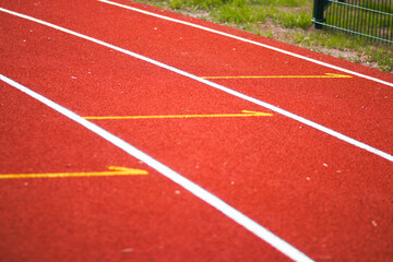Fototapeta premium White lane markings on a red running track at an athletics stadium. The textured rubber surface and clear lines indicate starting positions. Shot in daylight, outdoor setting.