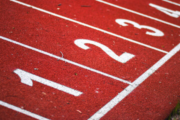 Fototapeta premium Numbered starting lines on a red running track at an athletics stadium, with a clear blue sky in the background.