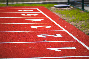 Numbered starting lines on a red running track at an athletics stadium, with a clear blue sky in the background.

