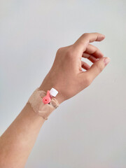 female hand with a catheter installed on the wrist, secured with a plaster. Light background, minimalism, medical theme, patient, hospital, inpatient