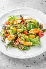 A colorful salad featuring mixed greens, cherry tomatoes, and soft-boiled eggs. This dish is both nutritious and visually appealing, perfect for a light meal or appetizer.