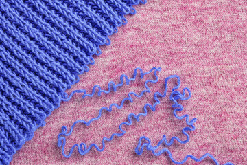 Unravelling blue wool knitted garment on pink background. Copy space