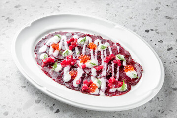 A beautifully presented dish of beetroot carpaccio drizzled with creamy sauce, garnished with fresh...