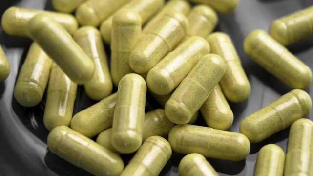 Green quercetin capsules with bromelain extract falling on black glass plate. Dietary supplement for immune support. Slow motion