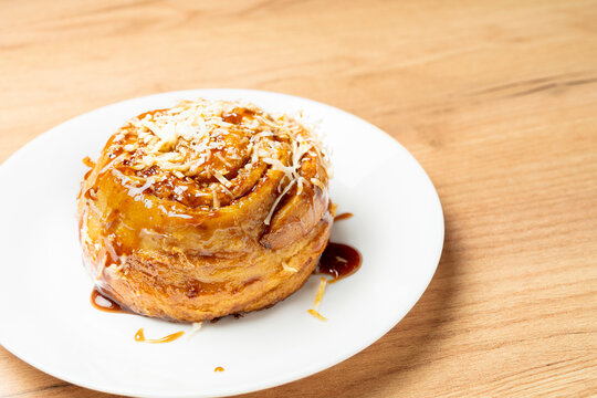 Freshly baked cinnamon roll topped with sweet caramel and grated cheese, sitting on a white plate- Golfeado with Cheese typical Venezuelan food.