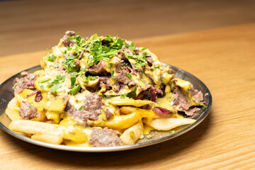 Close-up of loaded fries with shawarma meat, cheese sauce, and parsley on a metal plate