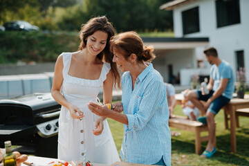 Adult daughter and mother preparing food for a family barbecue.