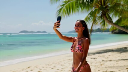 Young woman livestreams joyful selfie at tropical beach with palm trees and ocean waves in bright sunshine - Powered by Adobe