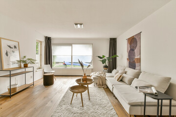 A stylish, modern living room featuring neutral tones, a cozy sofa, decorative art, and natural light streaming through large windows, creating a serene atmosphere.