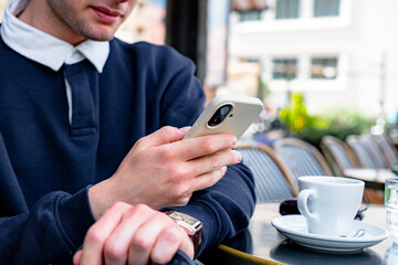 Close-up of a young man using his smartphone while enjoying a coffee at a traditional Parisian outdoor cafe