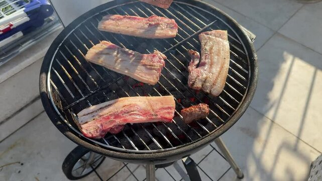 Sizzling pork belly and cevapcici on barbecue grill, professional chef carefully turning meat with spatula for perfectly even golden-brown cooking and maximum flavor