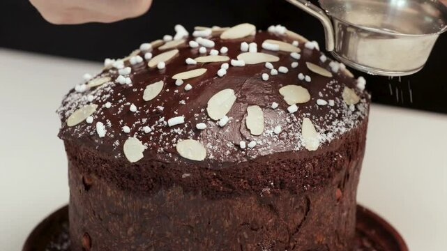 The cook decorates the panettone with powdered sugar. Baking for Easter and Christmas. Close-up of a woman's hands
