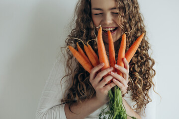 Portrait of smiling beautiful girl showing carrot on white background