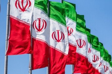 Multiple Iranian flags fluttering in the wind. Clear blue sky in the background