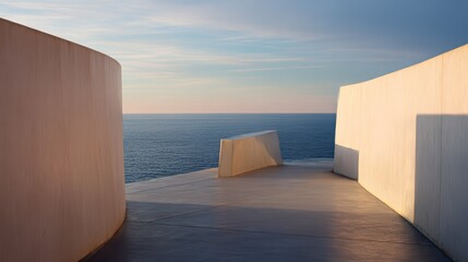 Modern coastal platform with geometric sculpture and curved walls overlooking ocean sunset.
