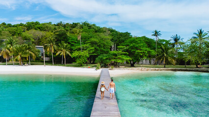 Couples stroll peacefully along the wooden pier, surrounded by lush greenery and turquoise waters at Koh Mak and Koh Kham Island in Thailand, capturing the beauty of this tropical paradise.