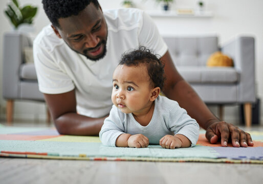 Father and baby enjoying tummy time together on a colorful play mat, creating a heartwarming moment of connection and early childhood development