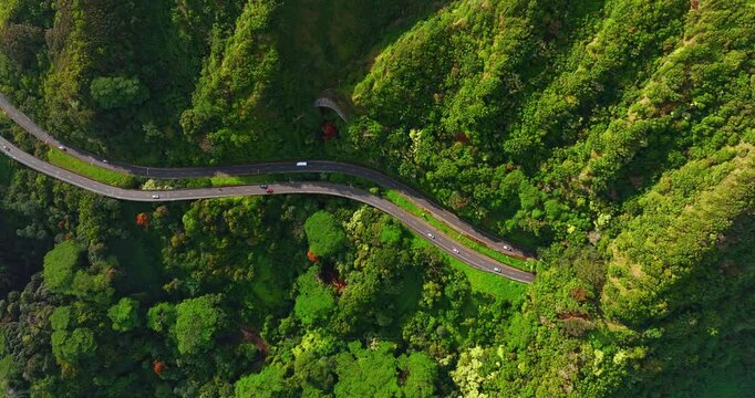 Automobiles ride by two highways crossing the green mountainous area. Drone footage above the roads and cars travelling by them.