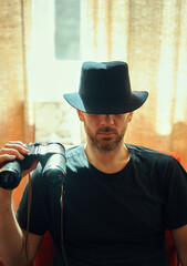 Mysterious man in black hat holding binoculars, sitting in front of window