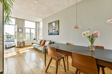 A stylish interior featuring a dining table with chairs, a cozy sofa, and large windows allowing natural light to brighten the room.