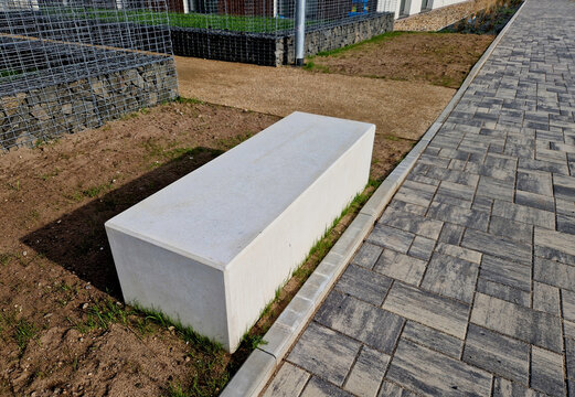 Concrete blocks with both sides shaped like cubes are seats in the park. A massive park bench forms a small courtyard with a gravel path surrounded by flower beds.