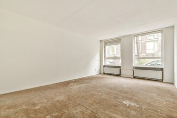 A vacant room featuring two windows allowing ample natural light, highlighting the bare walls and floor. An ideal space for decoration or remodeling.
