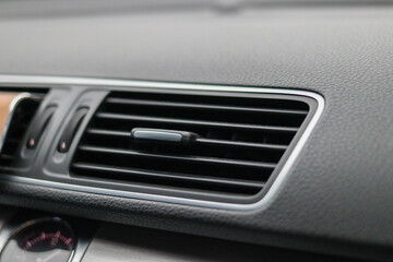 Close-up of a modern car air vent with horizontal slats and control knob, built into a textured black dashboard, showing detail of vehicle interior ventilation system. High quality photo
