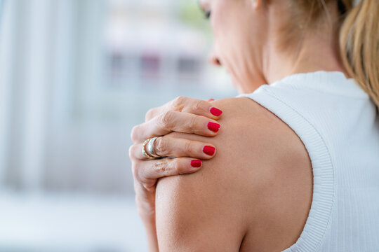 A woman experiencing shoulder pain, touching her sore muscles with discomfort. The image highlights tension, muscle strain, or possible injury, often caused by poor posture, stress, or overuse.