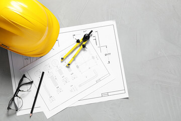 Different engineering drawings, hard hat, pencil, divider and glasses on grey table, flat lay....